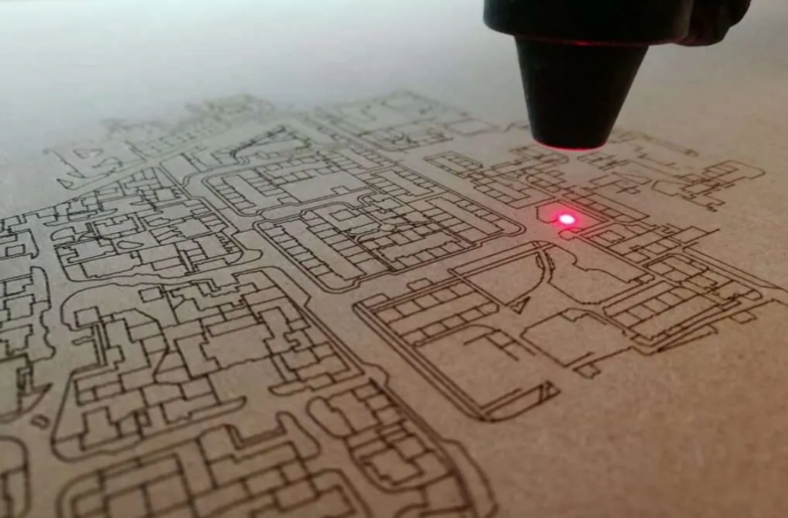 Favism3D: Grabado láser de precisión con optimización de materiales y reducción de residuos. Cabezal de láser grabando con alta precisión un mapa detallado sobre cartón, demostrando mínima generación de residuos.