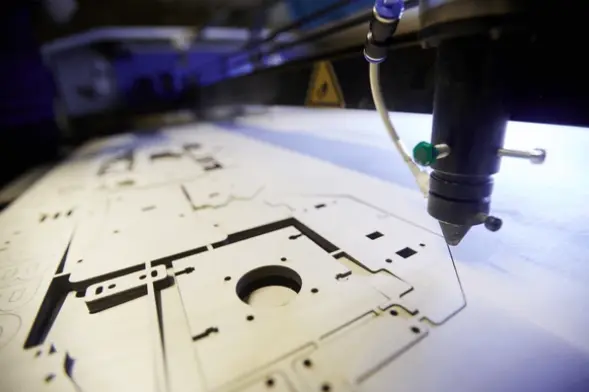 Favism3D: Servicios de corte láser de alta precisión para diseños personalizados y prototipado rápido. Máquina de corte láser industrial procesando un diseño complejo sobre madera, mostrando precisión en fabricación digital.